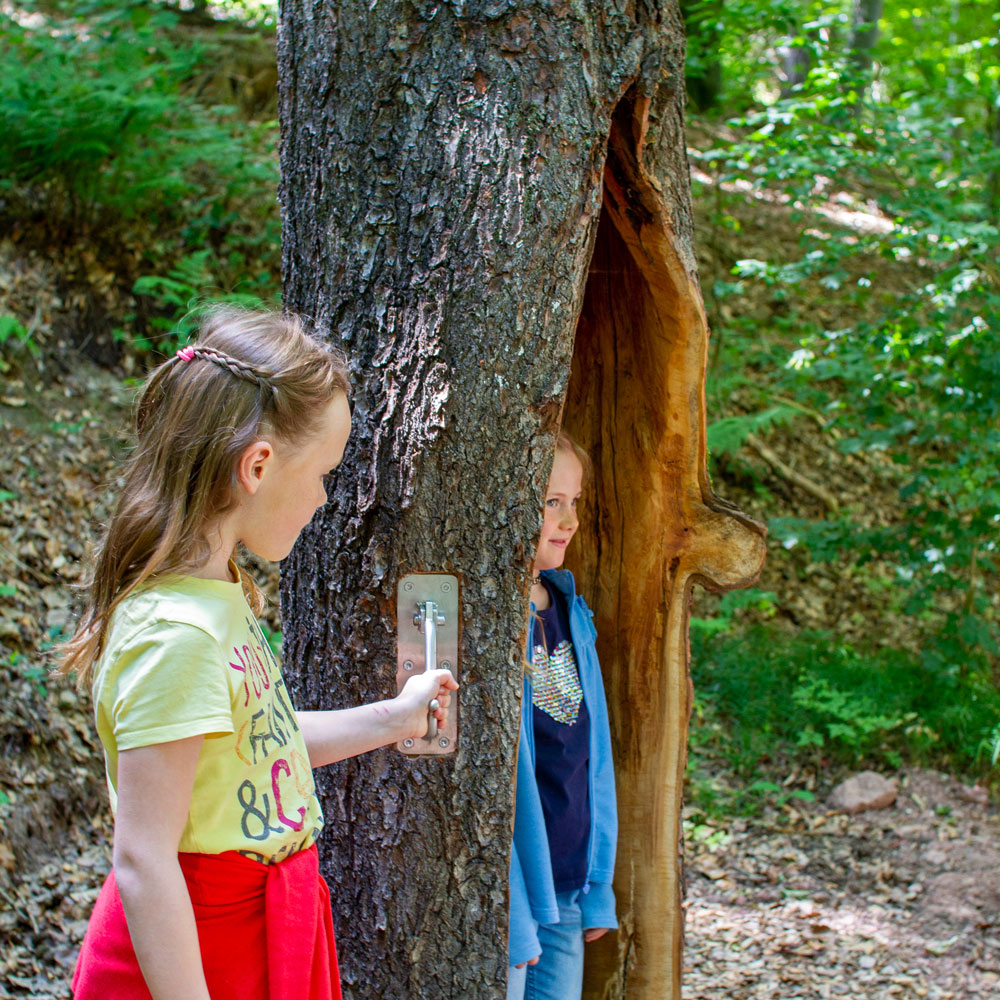 Kind steht im hohlen Baum, ein anderes Kind klopft außen und ahmt einen Specht nach